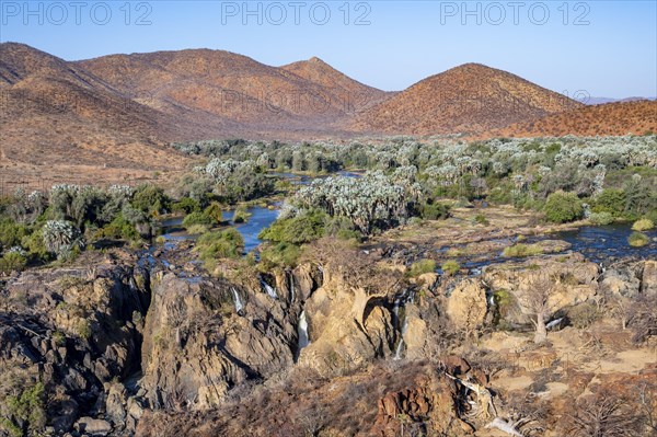 Kunene River with green vegetation in dry red mountain landscape, waterfall and African Baobab