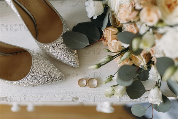 Silver shoes and wedding rings on a white table next to a bouquet of flowers