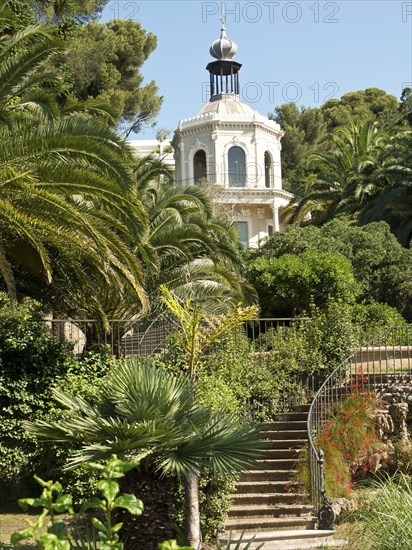 A magnificent villa surrounded by lush gardens and palm trees under a clear sky, la seyne sur mer,