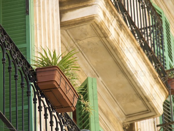 A balcony with decorative lattices, green shutters and a flower pot on a beige-coloured facade,