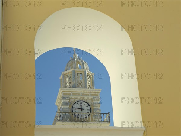 The clock of a church tower seen through a yellow arch, contrasted against the blue sky in