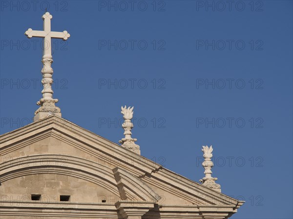 Top of a church with a cross and classical style elements in front of a cloudless blue sky, the old