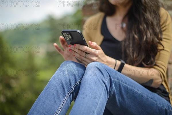 Young woman in casual clothing focused on conversation with smartphone in a peaceful garden with