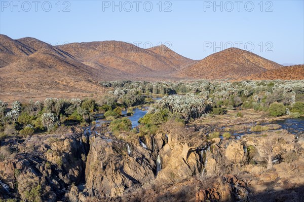 Kunene River with green vegetation in dry red mountain landscape, waterfall and African Baobab