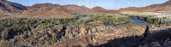 Panorama, Kunene River with green vegetation in dry red mountain landscape, waterfall and African