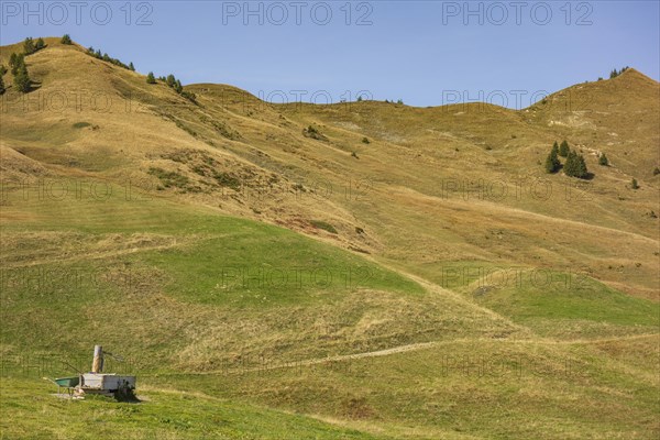 Abandoned hut on rolling green hills under a clear sky, rural and peaceful surroundings, mountain