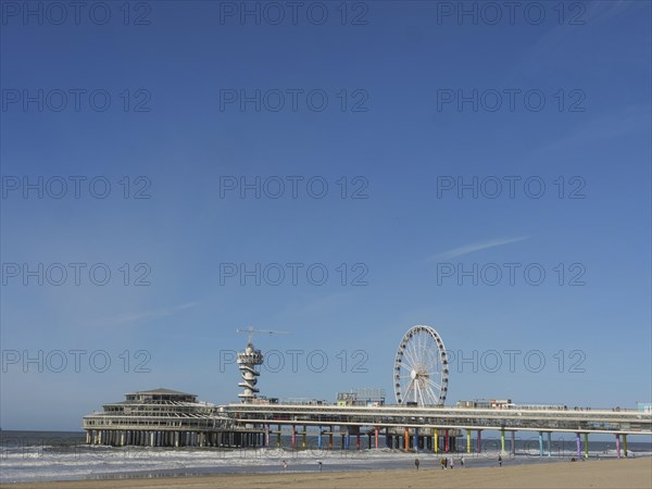 Pier with Ferris wheel and tower on the beach, sea in the background under a blue sky, parasols and