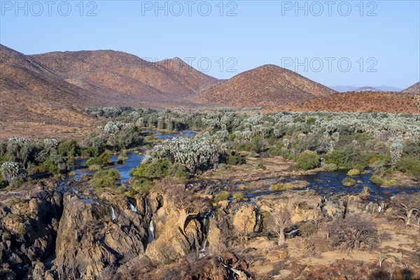 Kunene River with green vegetation in dry red mountain landscape, waterfall and African Baobab