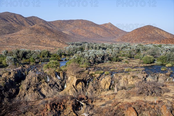 Kunene River with green vegetation in dry red mountain landscape, waterfall and African Baobab