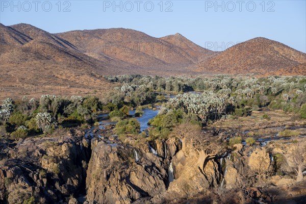 Kunene River with green vegetation in dry red mountain landscape, waterfall and African Baobab