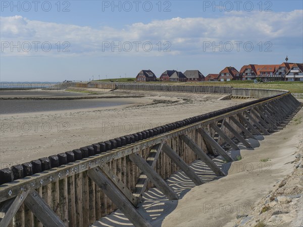 A beach with wooden constructions and houses in the background, sea and sky with some clouds,