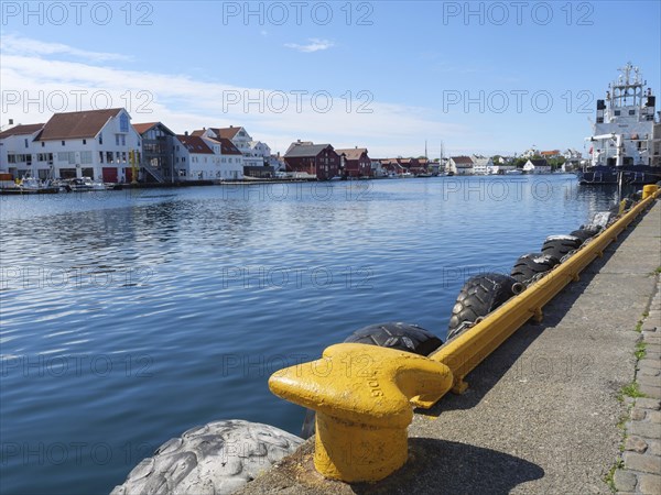 Waterfront with a yellow bollard and tyre protection, water and city in the background, in sunny