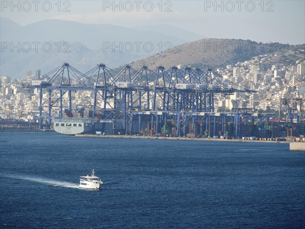 A large harbour with ships and containers, behind it a city and mountains, ancient buildings with