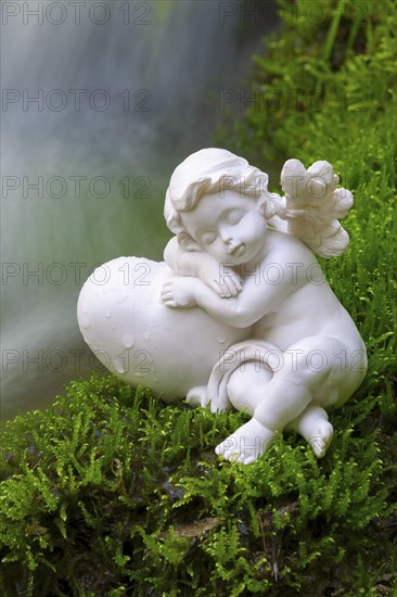 Porcelain angel figurine on moss by a waterfall