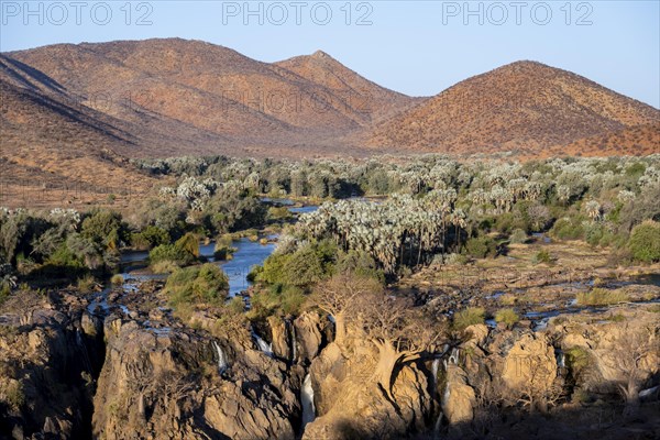 Kunene River with green vegetation in dry red mountain landscape, waterfall and African Baobab