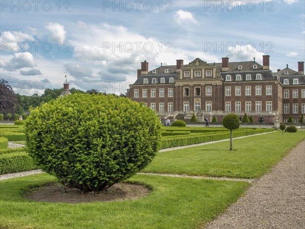 Well-kept symmetrical garden with hedges and paths in front of a historic castle under a cloudy
