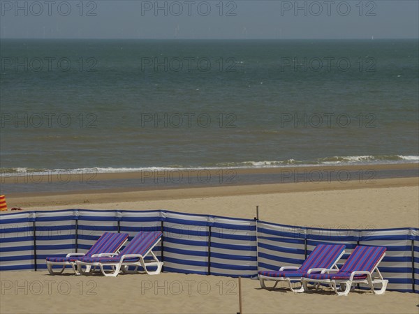 Wide view of a beach with blue and white striped deckchairs and a calm sea in the background,