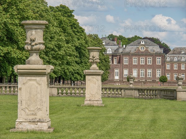 Two stone sculptures on lawn in front of an impressive historical building, surrounded by trees and