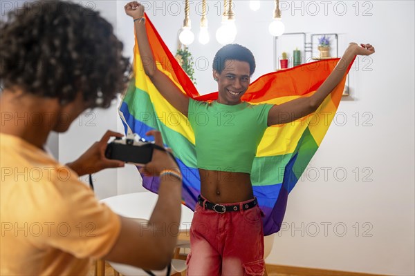 Gay man posing sensual with LGBT flag at home with his partner taking photos