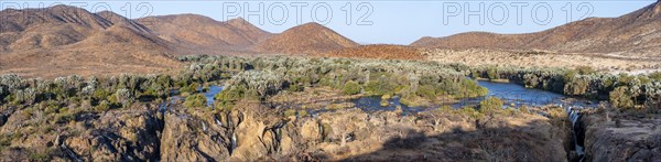 Panorama, Kunene River with green vegetation in dry red mountain landscape, waterfall and African