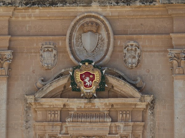 A detailed coat of arms on an old stone wall, surrounded by ornaments and reliefs, the town of