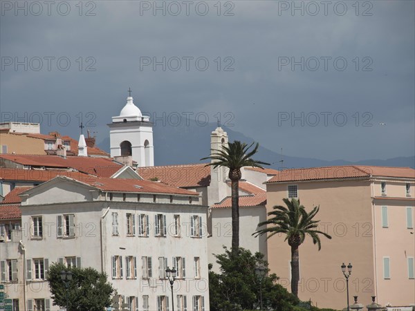 Mediterranean town with white buildings, a church tower and palm trees against a cloudy sky and