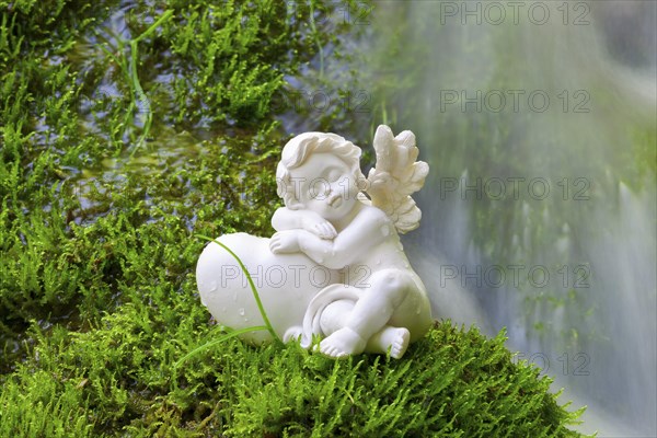 Porcelain angel figurine on moss by a waterfall