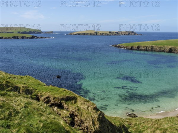Turquoise waters meet rocky cliffs and green grasslands under a blue sky, Green meadows by the sea