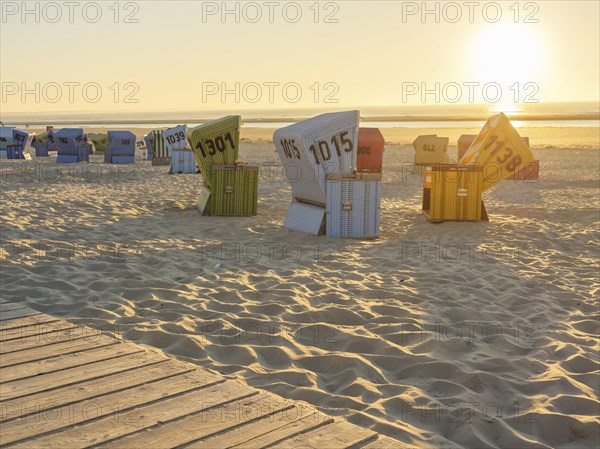 Several colourful beach chairs standing in order in the sand while the sun illuminates the horizon,