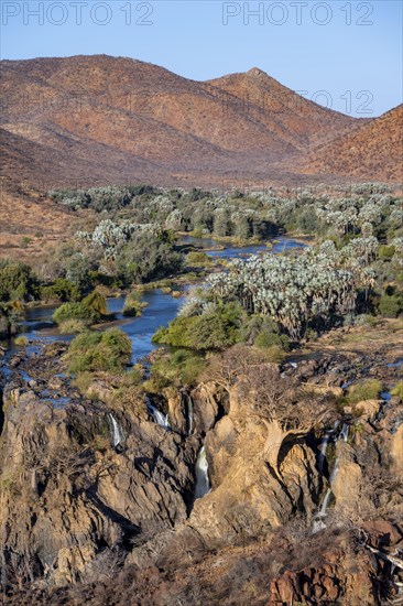 Kunene River with green vegetation in dry red mountain landscape, waterfall and African Baobab