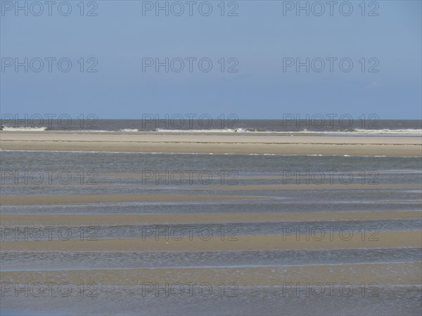 Empty beach at low tide with strips of sand and water under a blue sky, Baltrum Germany