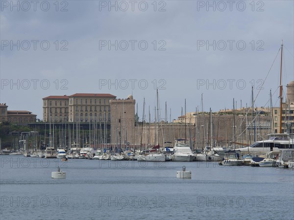 A harbour full of boats and yachts with historic buildings and sailing masts in the background,