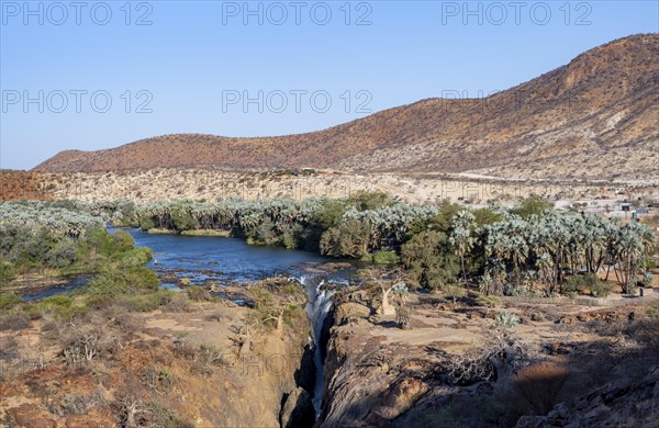 Kunene River with green vegetation in dry red mountain landscape, waterfall and African Baobab