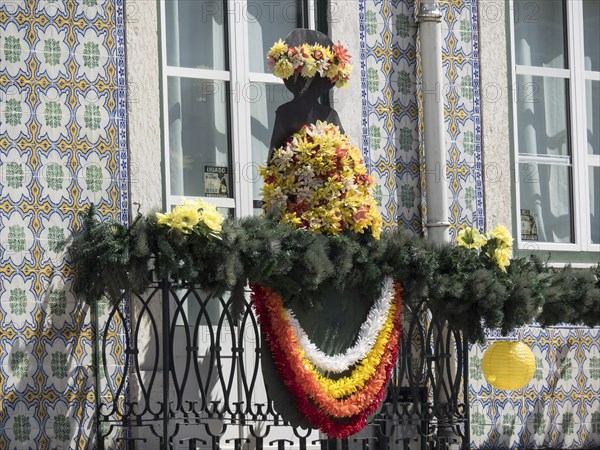 Colourful floral decoration on an ornate balcony with statue and tiles in the background, Lisbon,