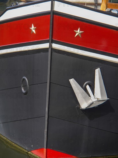 Detailed view of the bow of a black painted ship in the harbour with a large anchor, historic