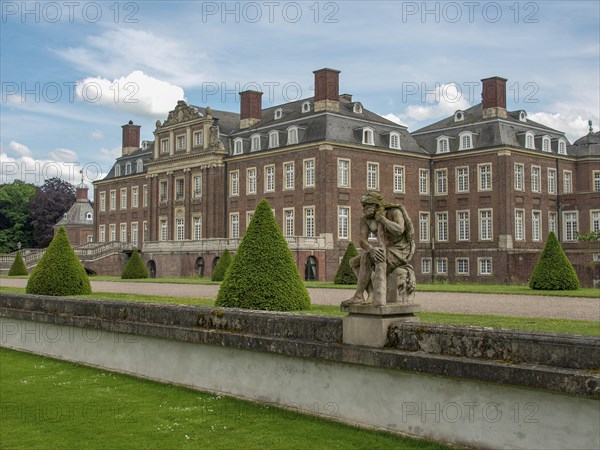Historic castle with manicured lawn, statues and bushes under a cloudy sky and spacious entrance,