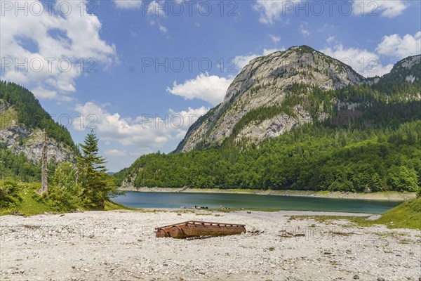 Rusted piece of metal on the shore of a lake with mountains in the background, turquoise green