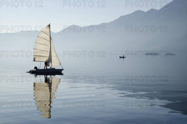 Old Sailing Boat Reflected on Lake Maggiore with Brissago Islands and Mountains in a Misty Sunny