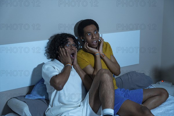 Gay couple watching a scary horror movie at night sitting at home