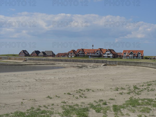 A sandy beach with a row of houses behind it under a blue sky with clouds, Baltrum Germany