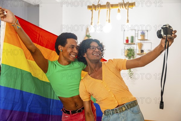 Happy gay couple celebrating diversity taking selfie at home raising LGBT rainbow flag