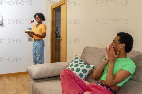 Gay latin young man surprising his partner with cake and a rose at home