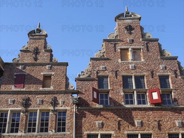 Historic red brick buildings with ornate facades and turrets under a clear blue sky, red brick