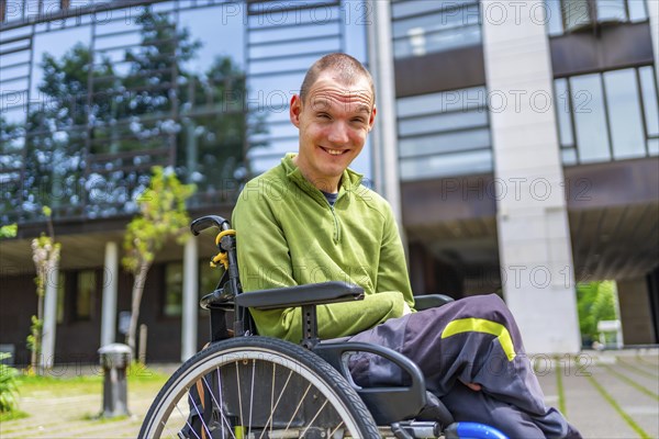 Happy disabled caucasian adult man in wheelchair smiling at camera outside the university
