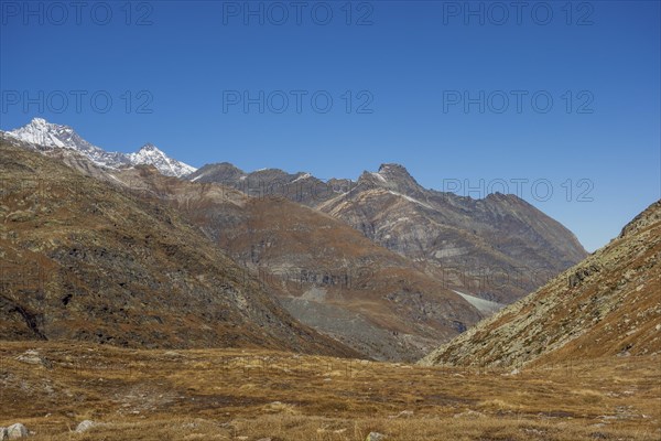 Vast valley between rocky mountains and mountain range under a bright blue sky, bare mountain peaks