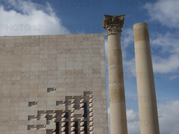 Two columns in front of a modern building with a fragment of ancient architecture and a heavenly
