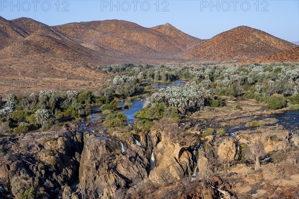 Kunene River with green vegetation in dry red mountain landscape, waterfall and African Baobab