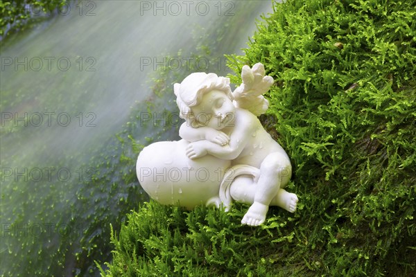 Porcelain angel figurine on moss by a waterfall