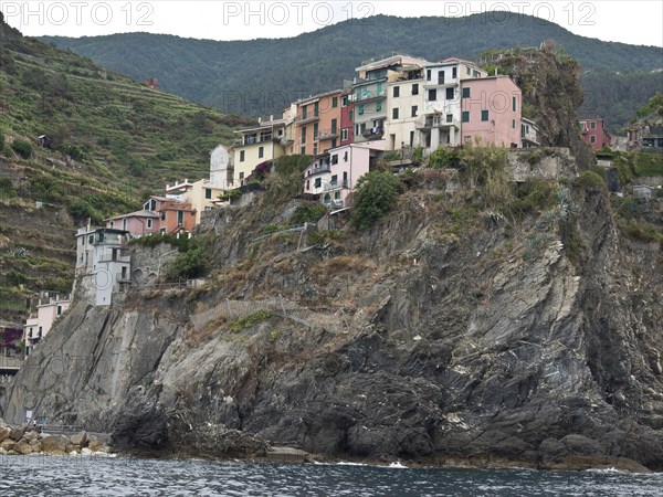 A village of colourful little houses clings to a rocky coastline surrounded by green hills, Bari,