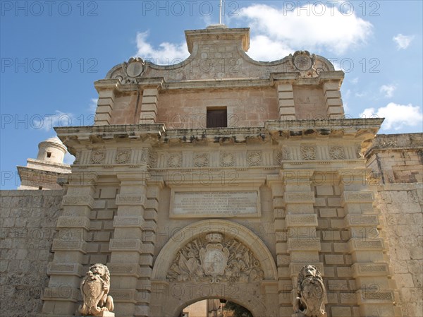 Monumental archway with lion statues, elegant sculptures and historic stone walls under a blue sky,